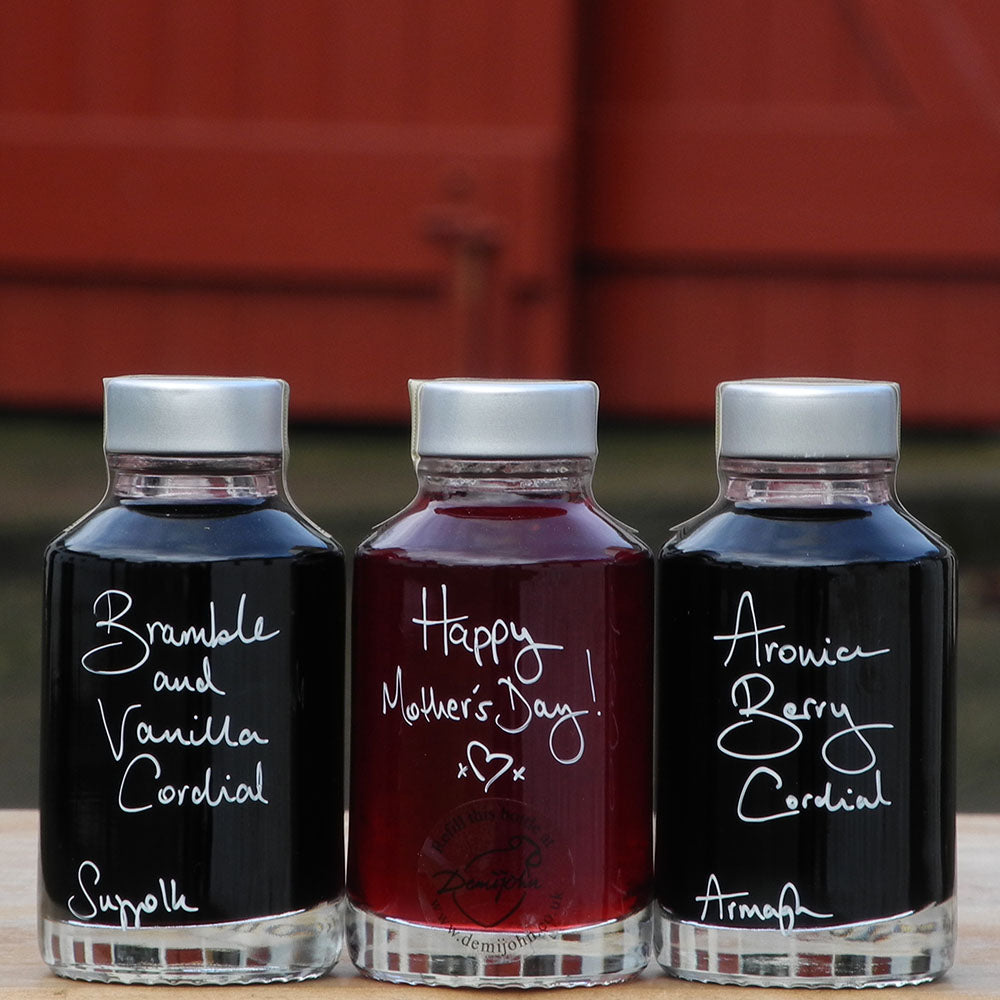 Seriously Fruity Alcohol Free Gift Set consisting of three 100ml bottles containing handmade Bramble and Vanilla Cordial, Raspberry Cordial and Aronia Berry Cordial with handwritten bottle labels in white pen that can be personalised, the middle bottle says 'Happy Mother's Day!' 