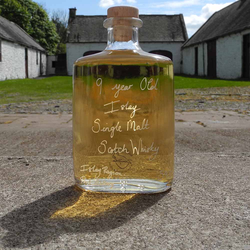 Hipflask shaped glass bottle of 9 year old Islay Single Malt Scotch Whisky on a concrete surface with traditional buildings in the background.