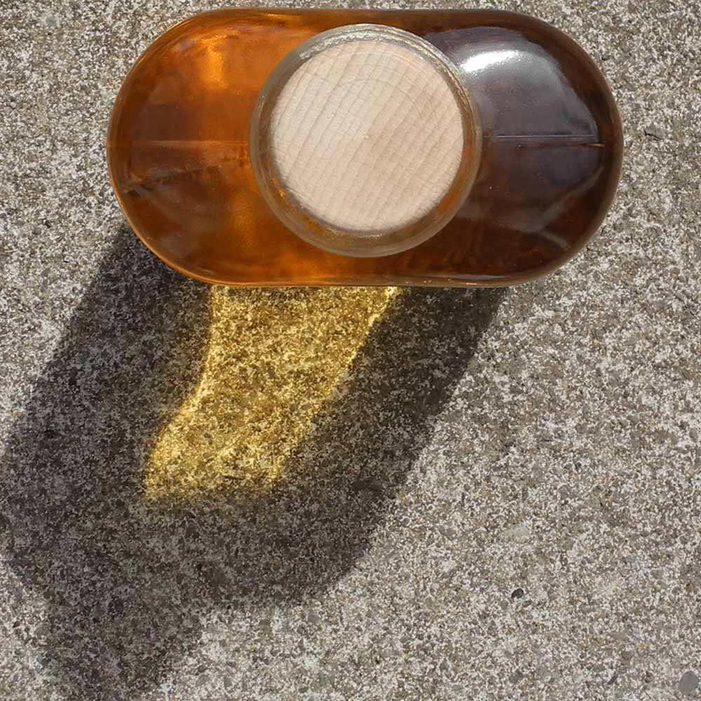 Top view of a bottle of Gooseberry Whisky Liqueur in a hipflask shaped glass bottle with a cork lid on a concrete surface.