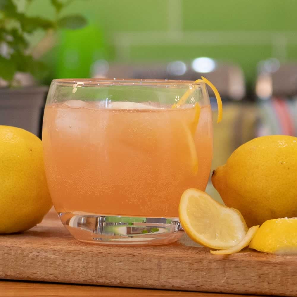 A tumbler glass with a Hold your Horses Cocktail in it surrounded by lemons